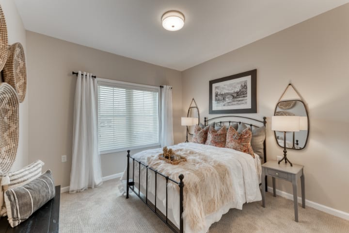 A cozy bedroom with neutral tones, featuring a neatly made bed, bedside lamps, and a large window.