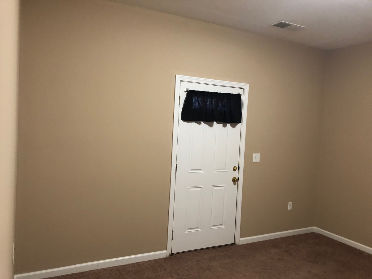 An interior room with a beige wall and a white door featuring a small black curtain.
