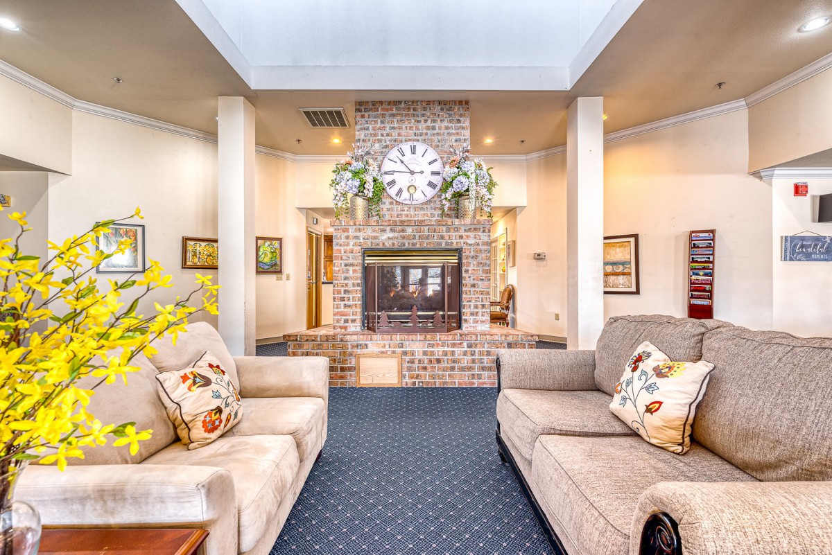 A cozy living room with a central fireplace, decorated with sofas and a large wall clock.