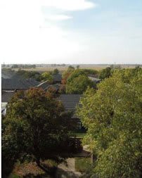 A scenic view of rooftops surrounded by lush green trees under a clear sky.