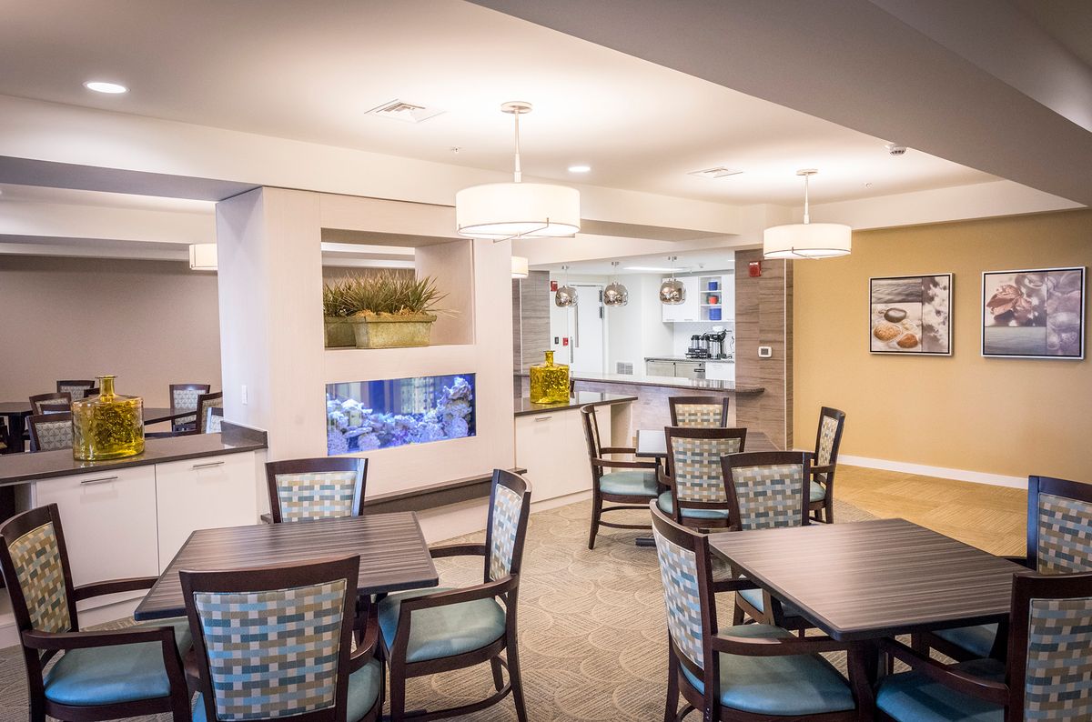 A well-lit dining area featuring tables and chairs, with an aquarium integrated into the wall.