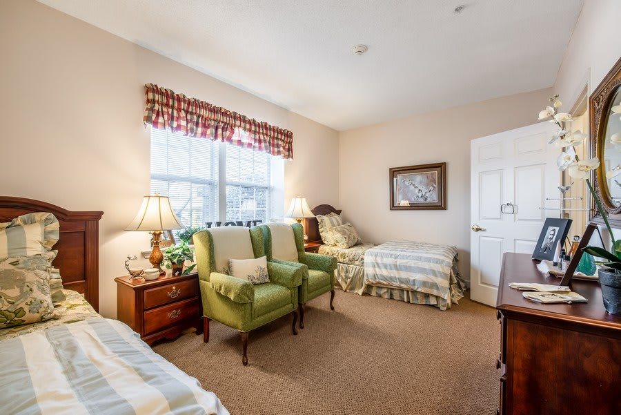 A cozy bedroom with twin beds, green armchairs, and warm lighting.