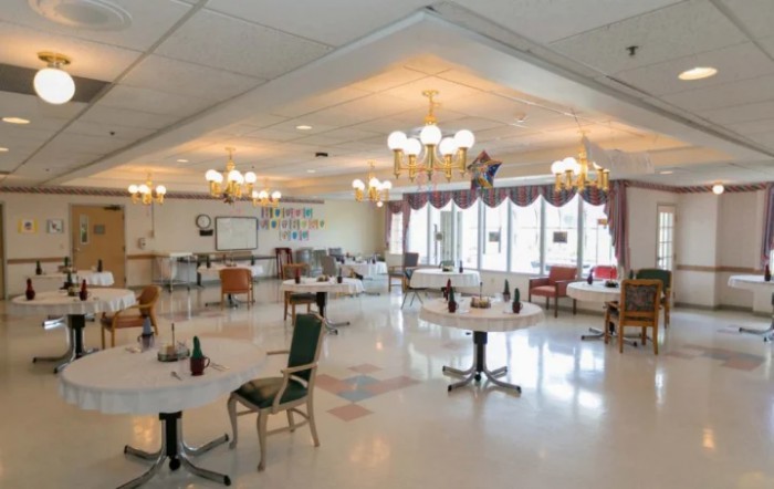 An empty dining area with tables and chairs, illuminated by chandeliers.