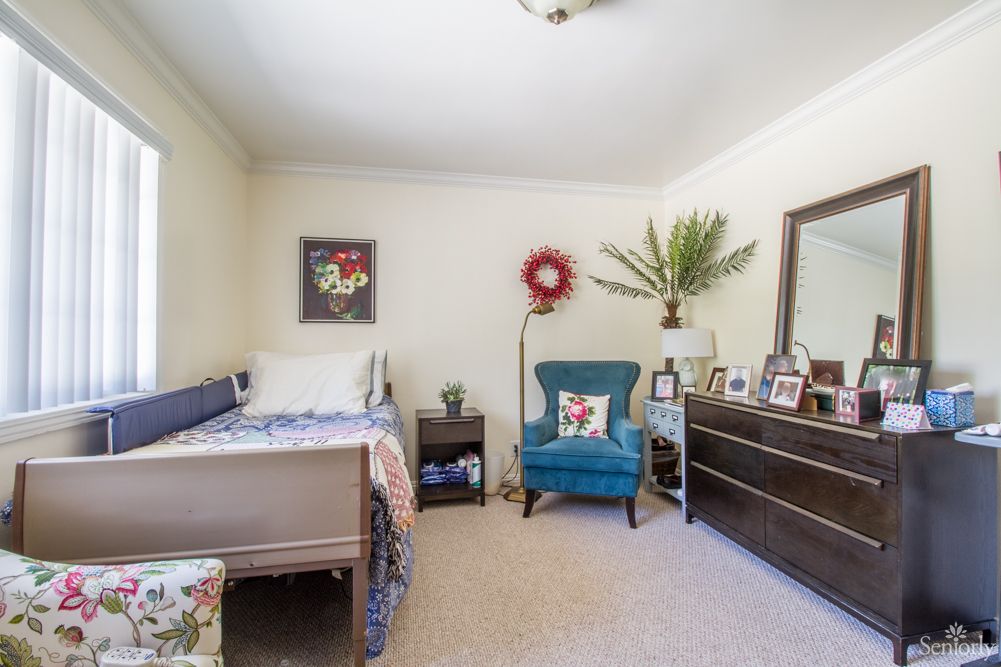 A cozy bedroom with a bed, armchair, dresser, and decorative elements.