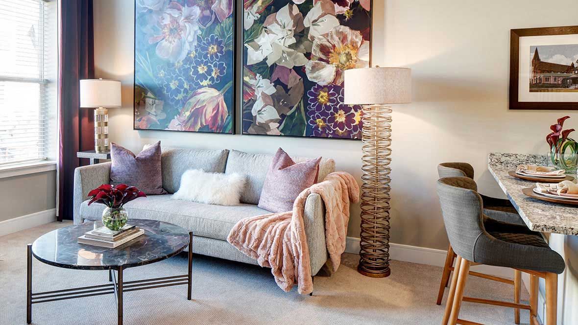 A cozy living room featuring stylish artwork, a comfortable sofa with accent pillows and a throw, accompanied by a unique floor lamp and glass coffee table.