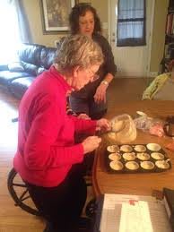 An elderly woman preparing cupcakes in a cozy kitchen setting.
