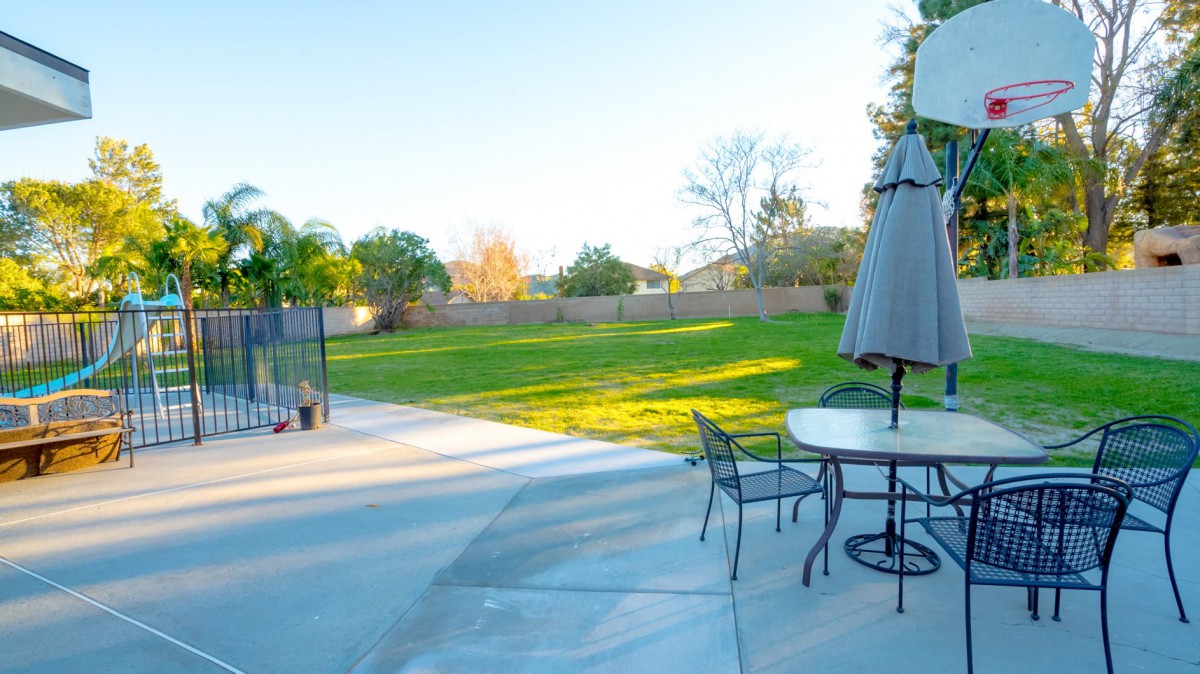 A spacious backyard with a patio set and umbrella overlooking a green lawn and trees.