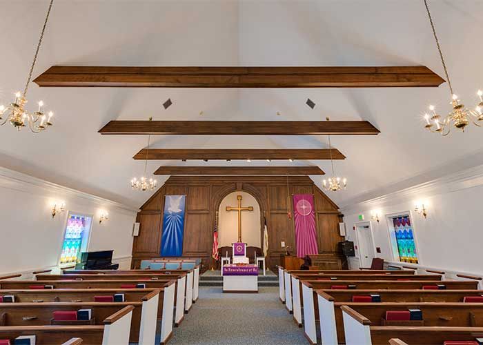 Interior view of a church with wooden pews and a prominent cross at the altar.