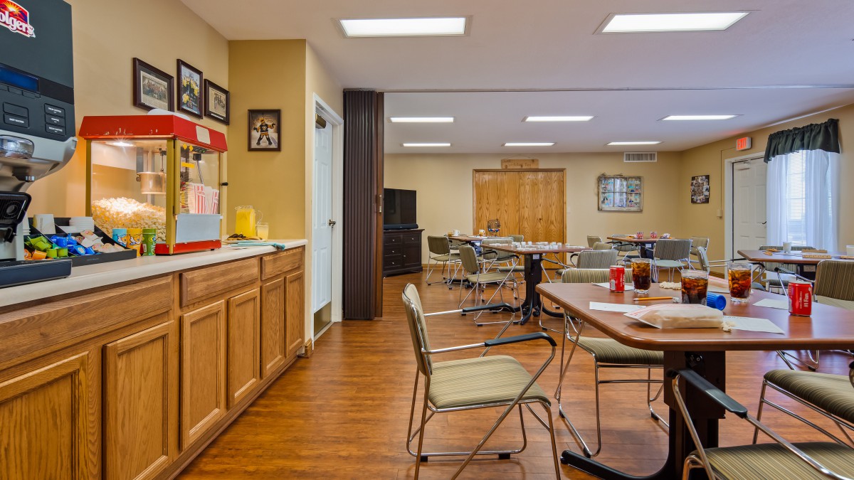 A community room with tables, chairs, a popcorn machine, and wood flooring.