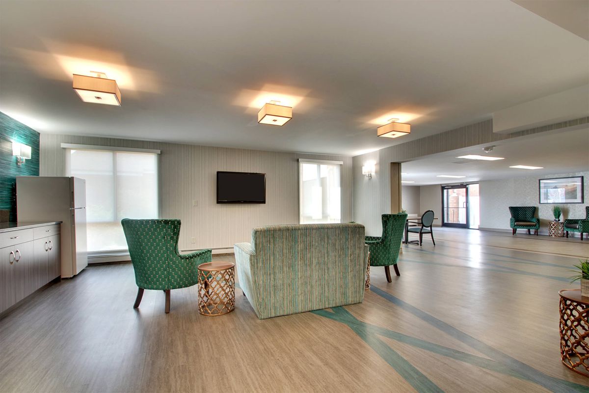 A modern living room with a sofa, green chairs, and a wall-mounted television.