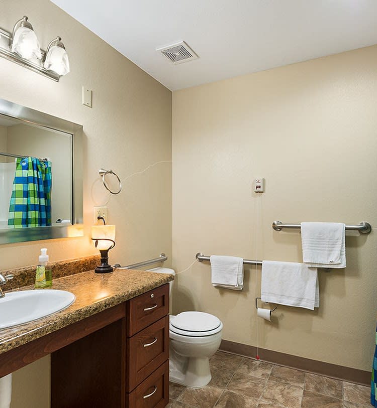 A well-lit bathroom with a sink, mirror, and towels neatly arranged.