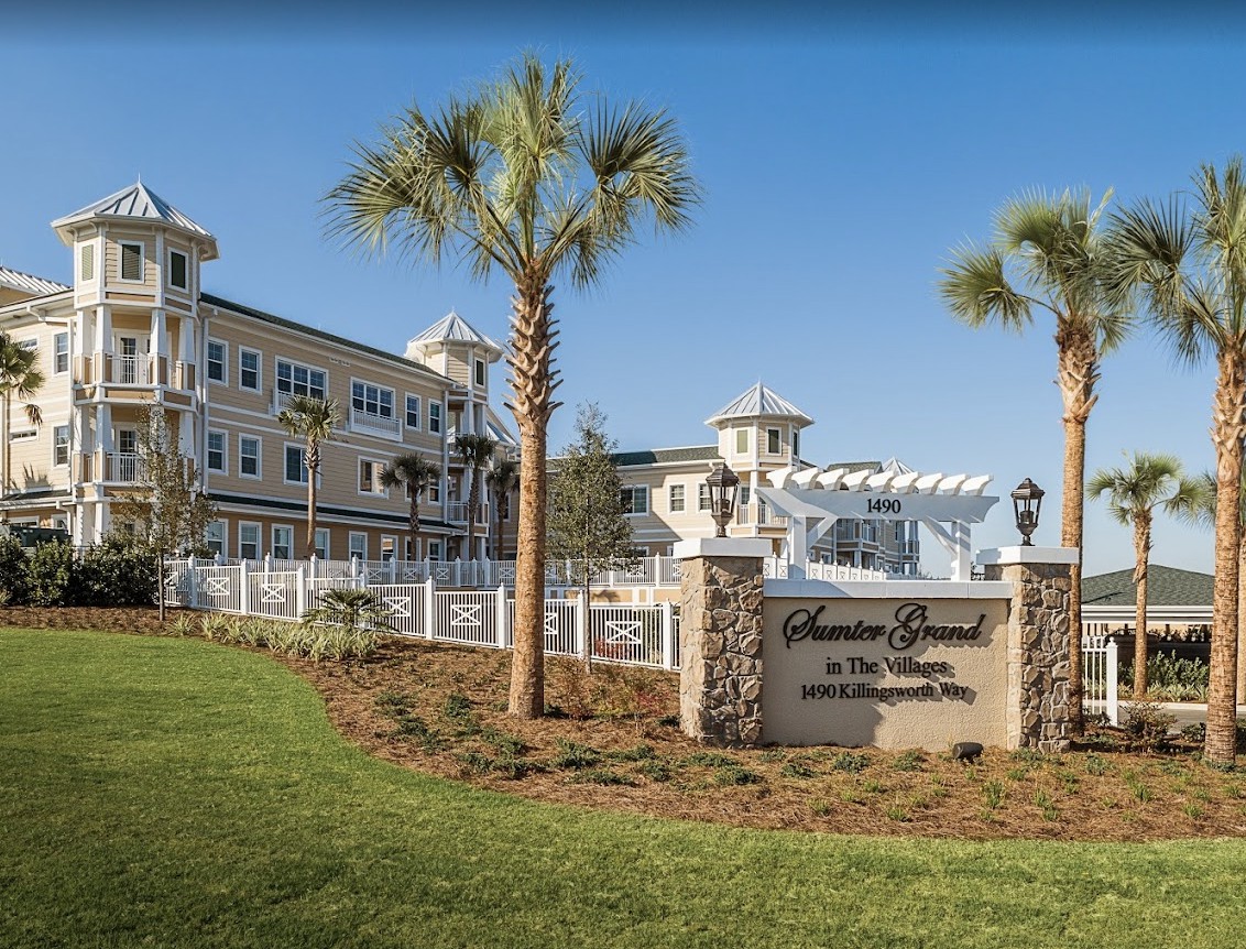 A scenic view of a large building with palm trees and a sign in front, set against a clear blue sky.