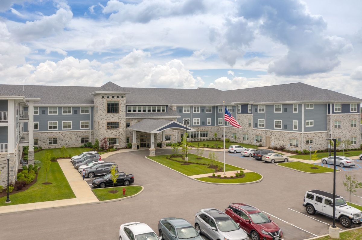 A large building with a parking lot and cars, featuring an American flag and a cloudy sky in the background.