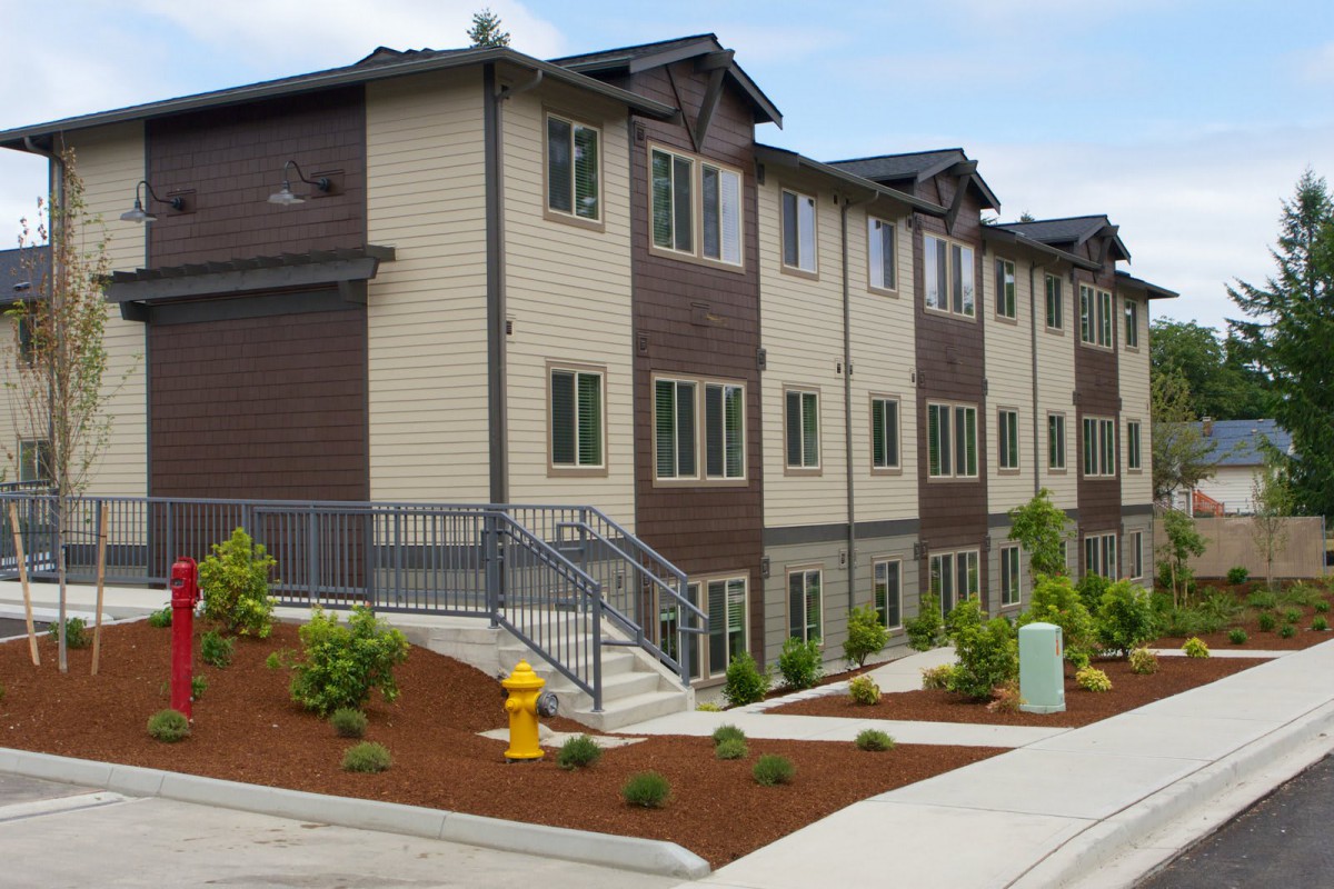 A modern apartment building with landscaped surroundings and a staircase leading to the entrance.