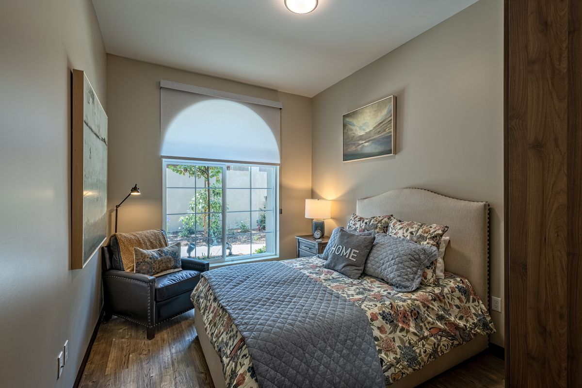 A cozy bedroom with a neatly made bed, a large window, and elegant decor.
