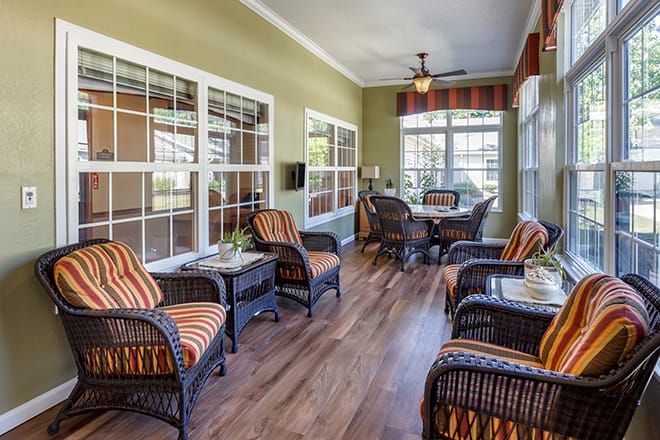 A cozy sunroom featuring wicker furniture and large windows overlooking a serene view.