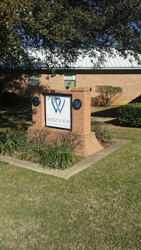 A brick sign displaying the logo and name of a building, surrounded by green landscaping.