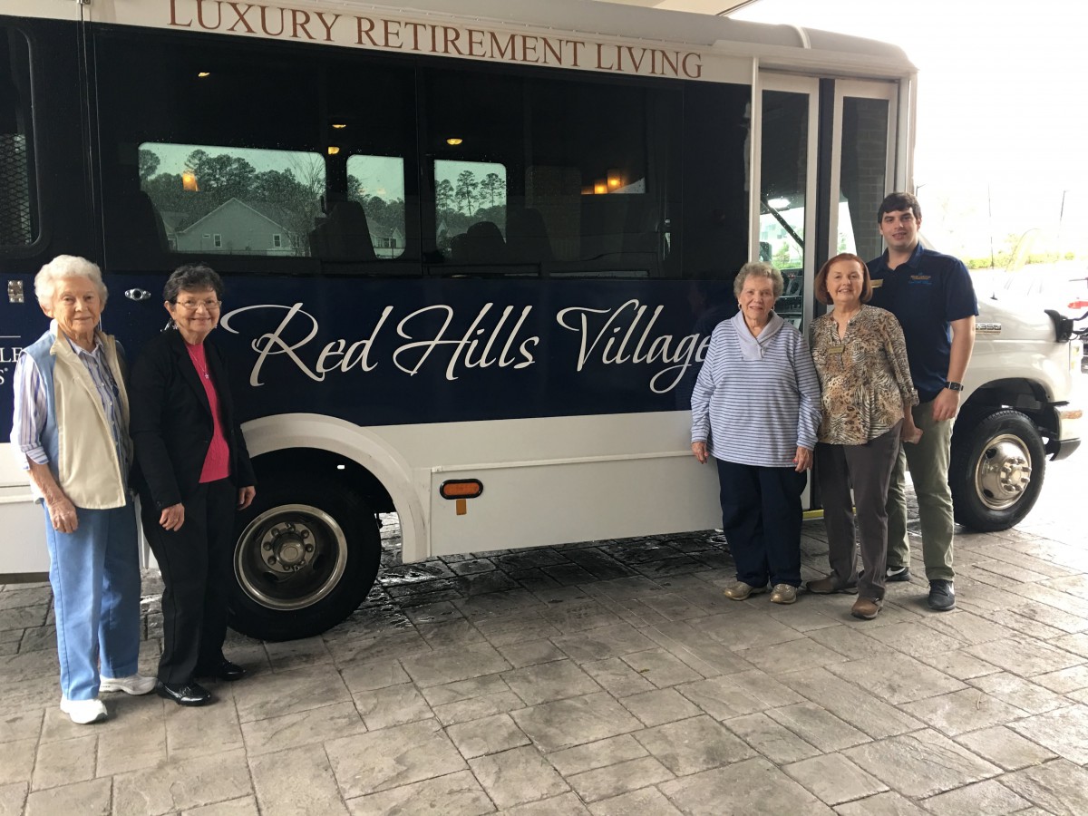 A group of people standing next to a bus with 'Red Hills Village' on its side.