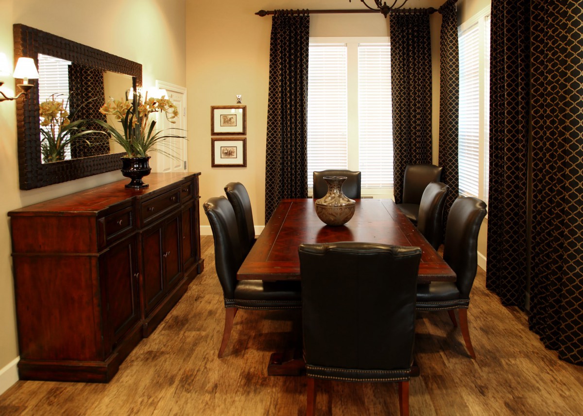 A stylish dining room with a wooden table surrounded by chairs, adorned with elegant decor and curtains.
