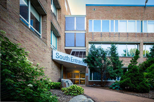 The south entrance of a modern brick building, featuring large windows and surrounding greenery.