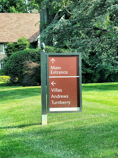 A directional sign indicating the main entrance and various villas in a well-manicured outdoor area.