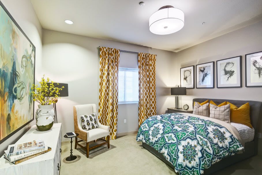 A modern bedroom with colorful bedding and patterned curtains.