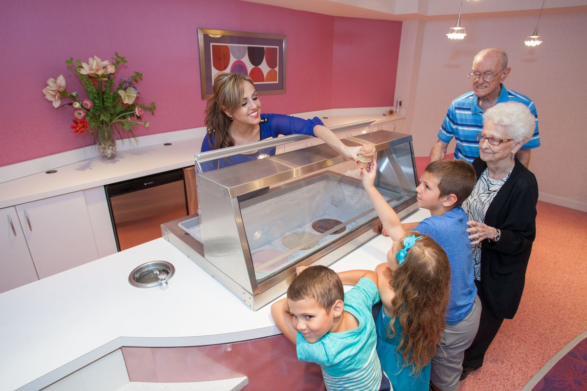 A group of children being served ice cream at a counter by a woman.