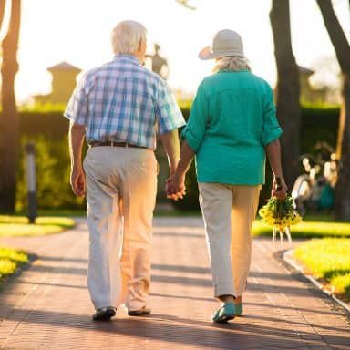 An elderly couple walking hand in hand in a park during sunset.