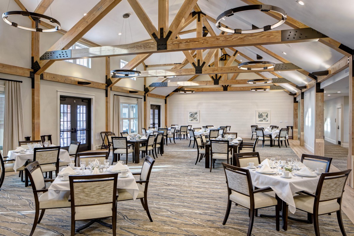 An elegant dining room with neatly arranged tables and chairs, featuring exposed wooden ceiling beams.