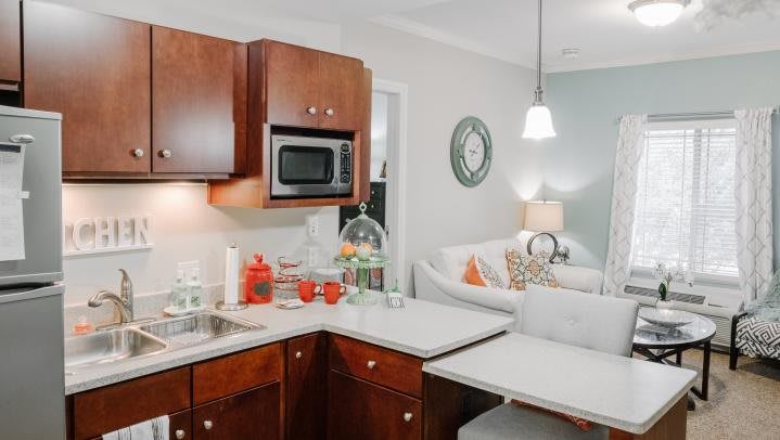 A modern kitchen with wooden cabinets, a microwave, and an open plan design leading to a cozy living area.