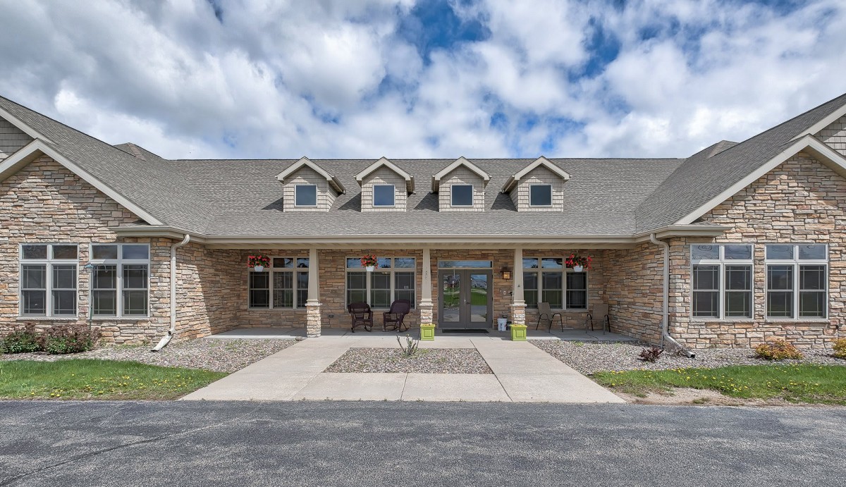 A spacious stone-front house with a gabled roof and large windows under a partly cloudy sky.