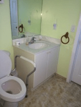 A small bathroom with a sink, toilet, and mirror, featuring green-painted walls and tiled flooring.