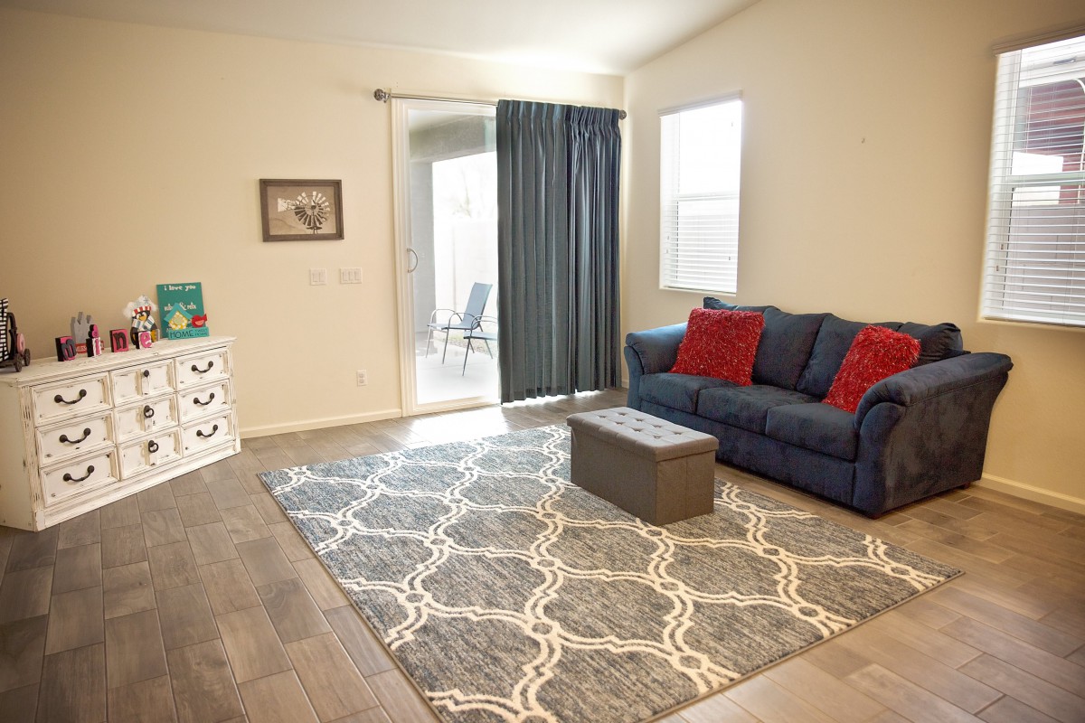 A cozy living room with a blue sofa and red pillows, featuring a patterned rug and dark curtains.