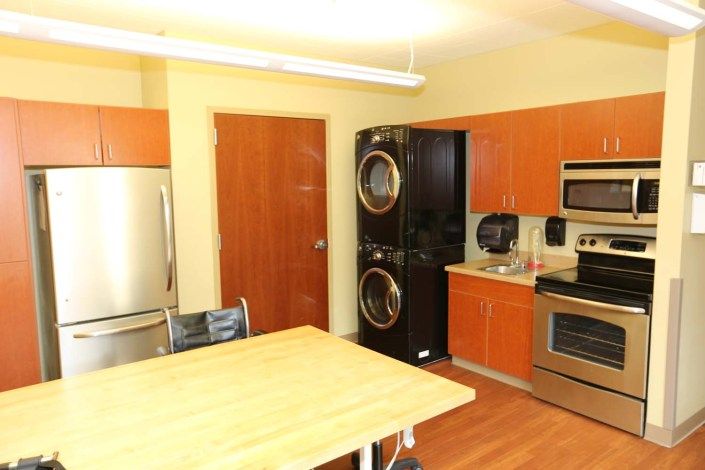 A modern kitchen featuring a stainless steel stove, microwave, and refrigerator, along with a stacked washer and dryer unit and a wooden table.