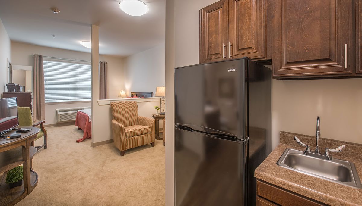 A cozy apartment interior featuring a kitchenette, fridge, and a comfortable living space with an armchair.