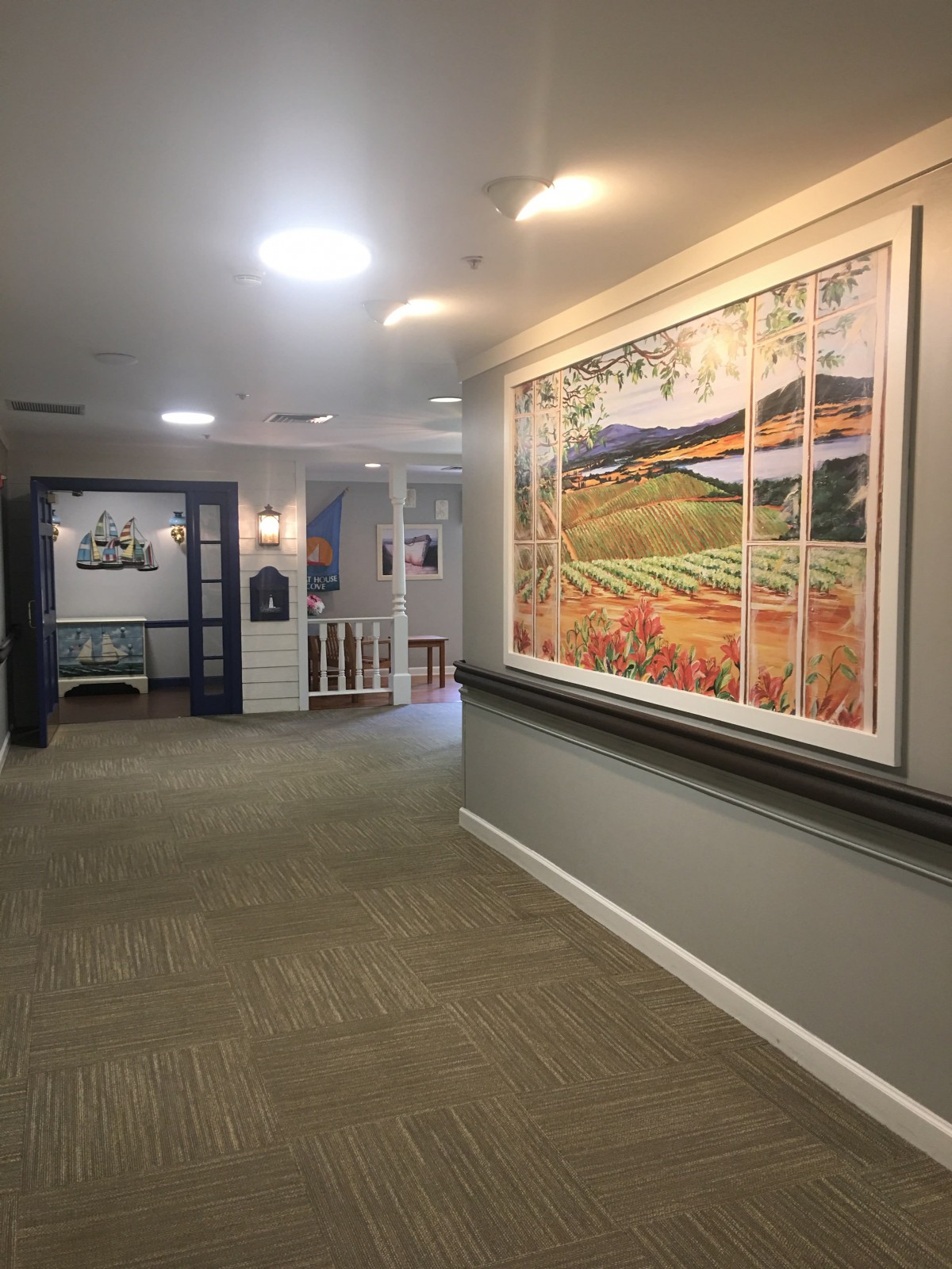 A well-lit hallway with a large framed painting on the wall and a carpeted floor.