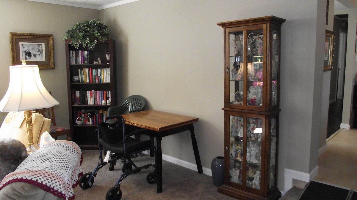 A cozy home office with a wooden desk, comfortable chair, bookshelf, and a glass display cabinet.