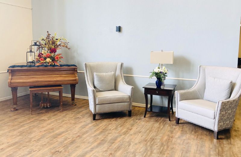 A cozy living room with two armchairs, a side table with a lamp, and a piano adorned with flowers.