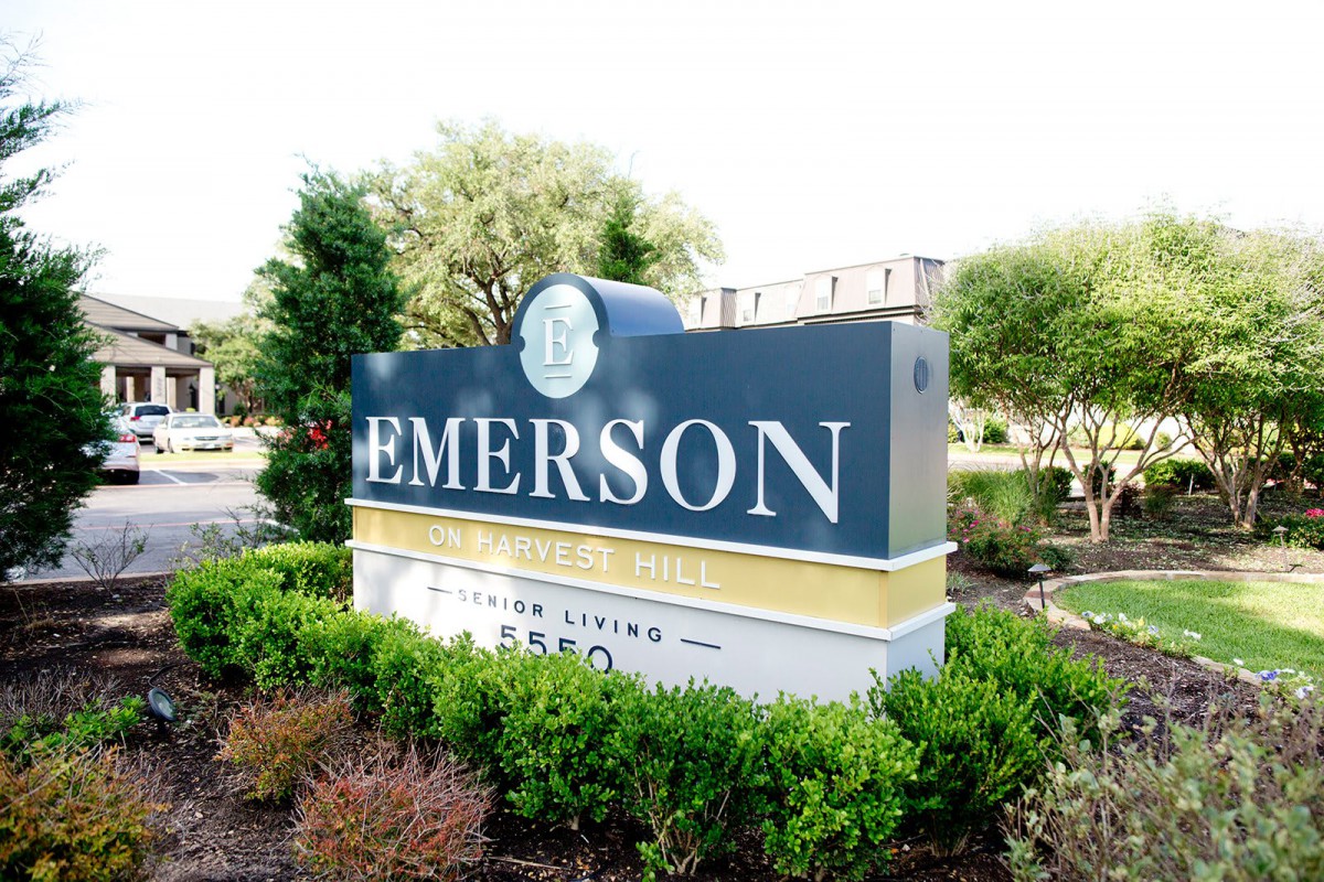The image shows an outdoor sign for Emerson, surrounded by greenery.