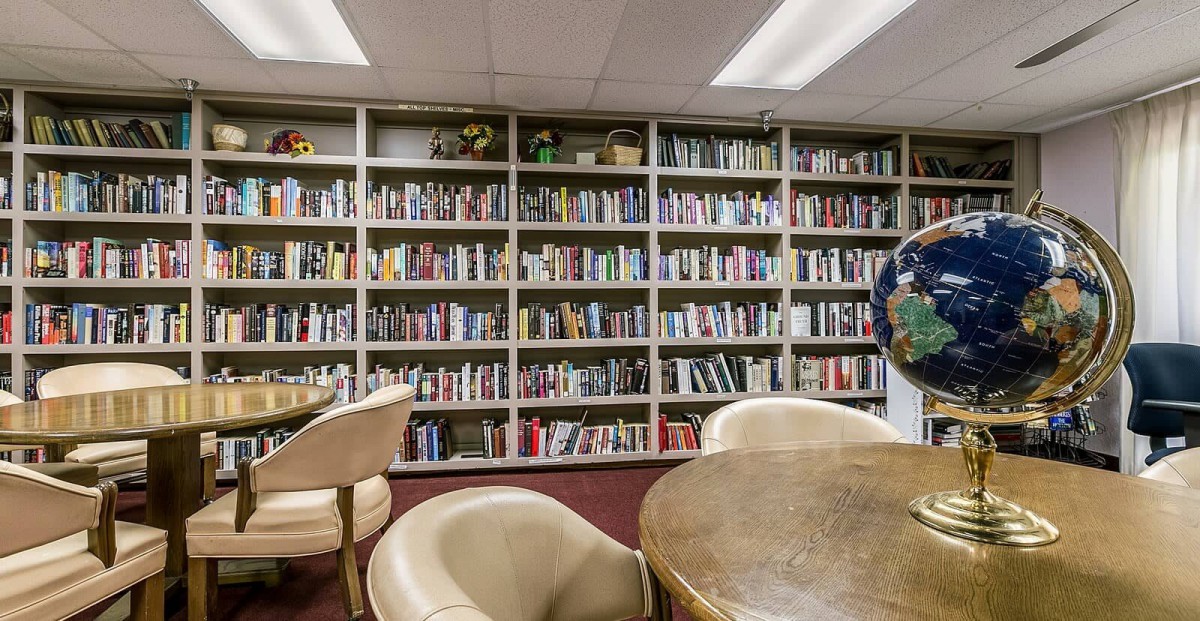 A cozy library room with bookshelves, chairs, and a table for reading.