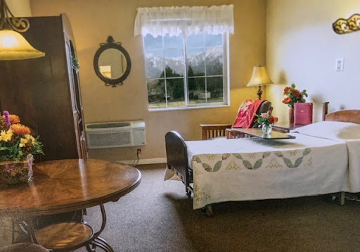 A cozy and well-lit bedroom featuring a neatly made bed, a round table, and a large window offering a glimpse of the outside.