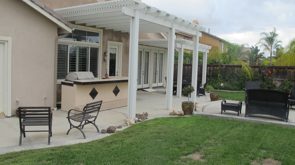 A backyard patio with a white pergola and outdoor kitchen setup.