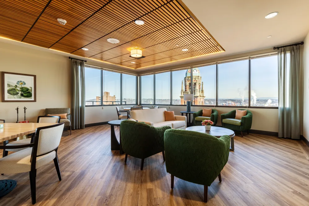 A modern lounge area with comfortable seating, large windows offering a city view, and warm wood design elements.