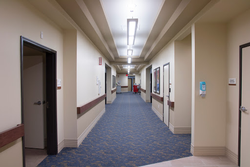 A well-lit corridor in a hospital, featuring doors to different rooms and a carpeted floor.