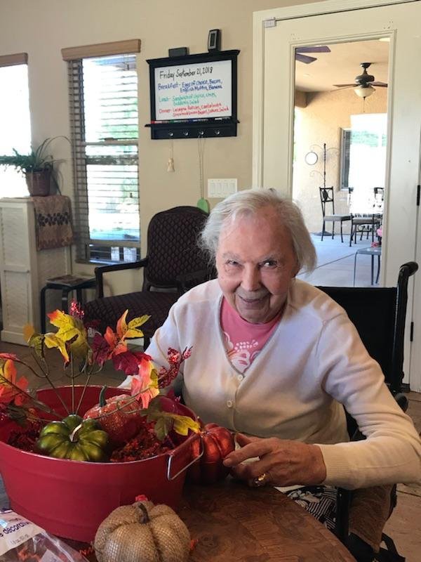 An elderly woman in a wheelchair enjoys crafting with autumn leaves indoors.