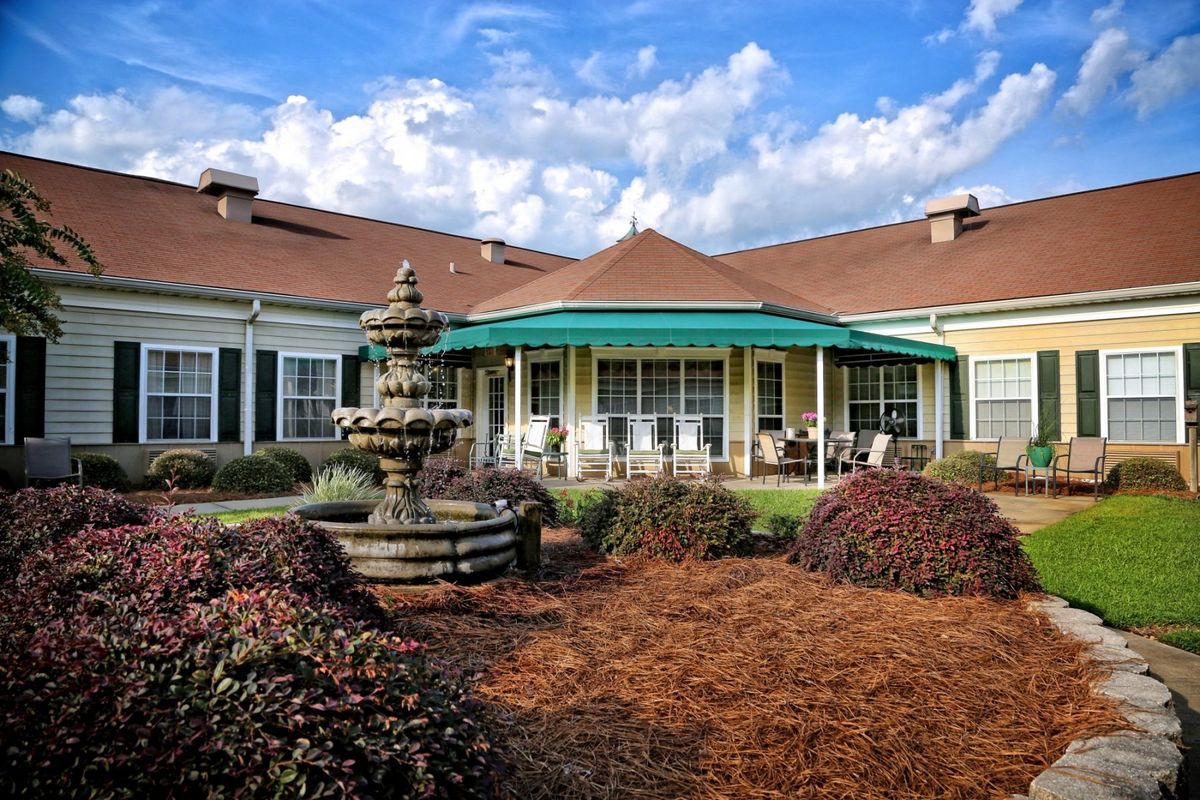 A scenic view of a building with a fountain and landscaped garden under a partly cloudy sky.