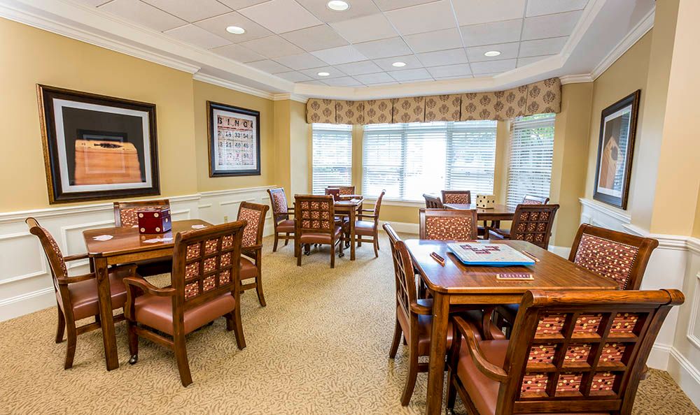 A well-lit dining area with several tables and chairs, featuring large windows and a carpeted floor.