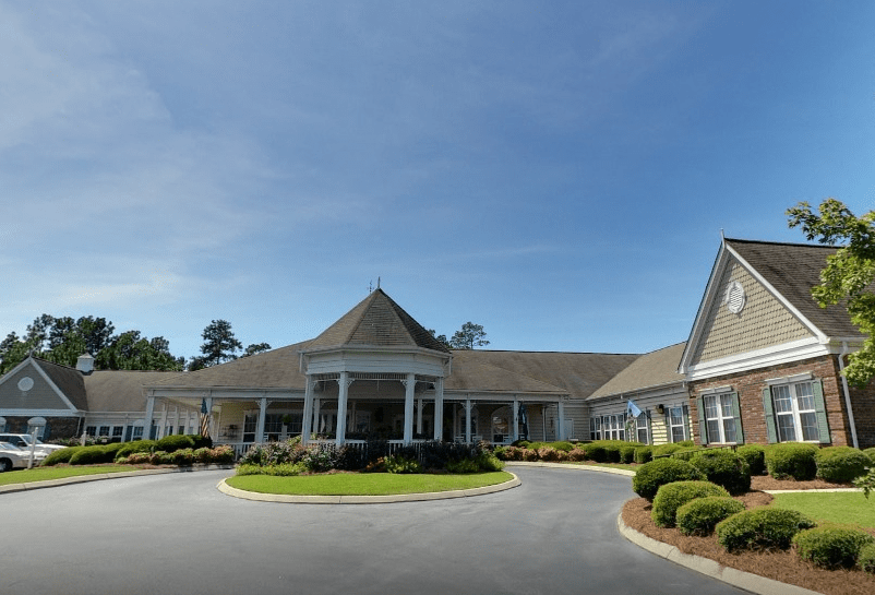 A large, elegant building with a circular driveway and neatly landscaped grounds under a clear sky.