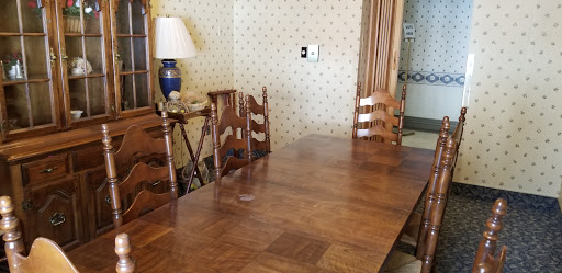 A cozy dining room featuring a wooden table and chairs, complemented by a lamp and patterned wallpaper.