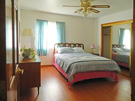 A cozy bedroom with a bed, ceiling fan, and a window with curtains.